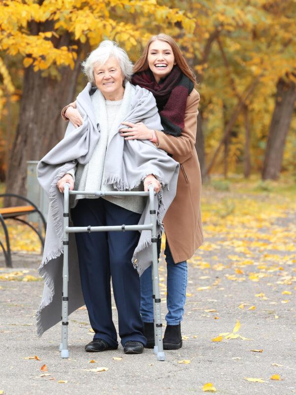 Senior Woman With Walking Frame And Young Caregiver In Park